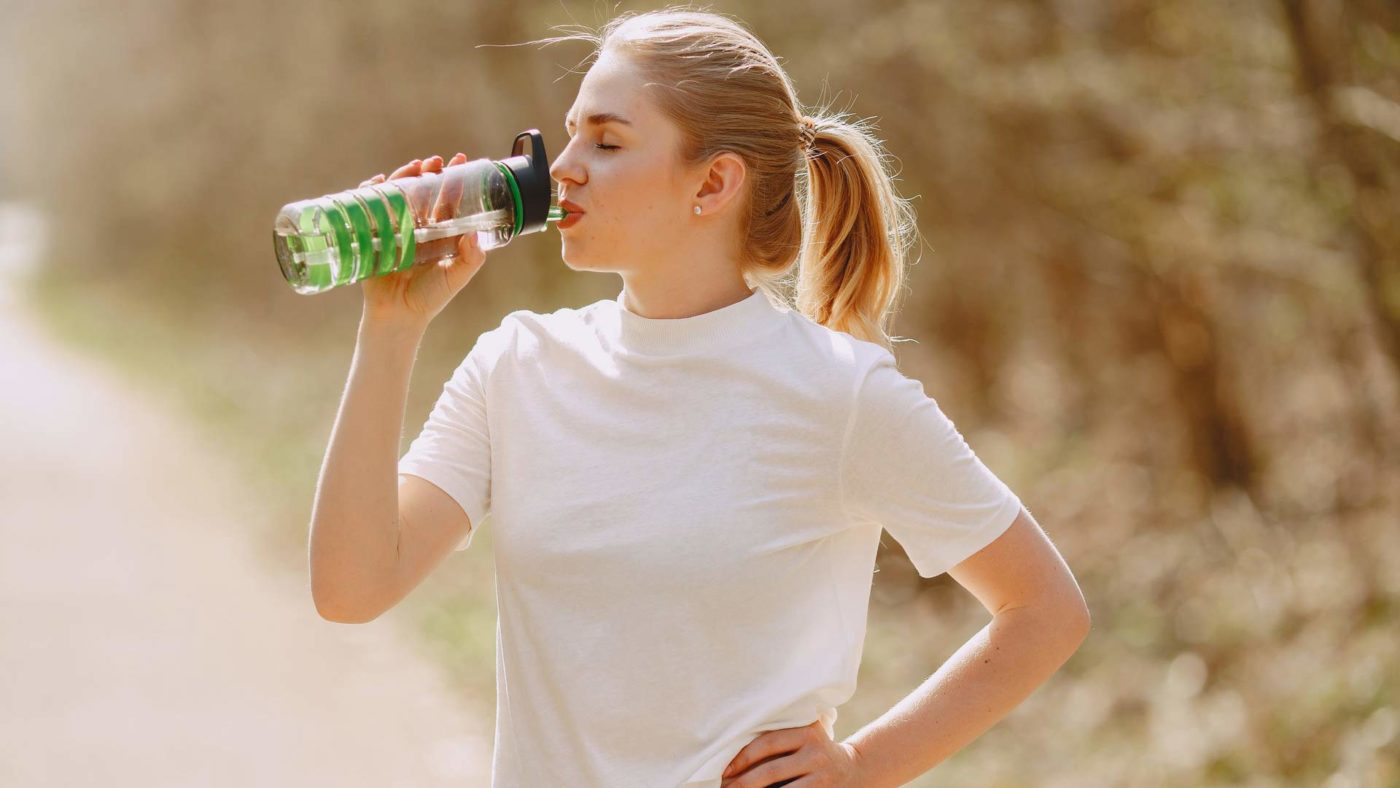 Woman drinking water from a reusable bottle in the nature